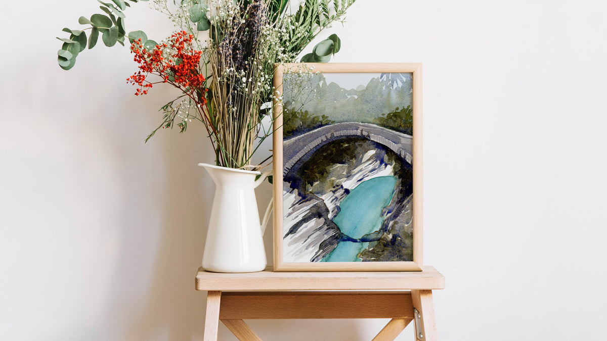 Gerahmter Fine-Art-Print einer handgemalten Aquarelllandschaft mit Steinbrücke und türkisfarbenem Wasser